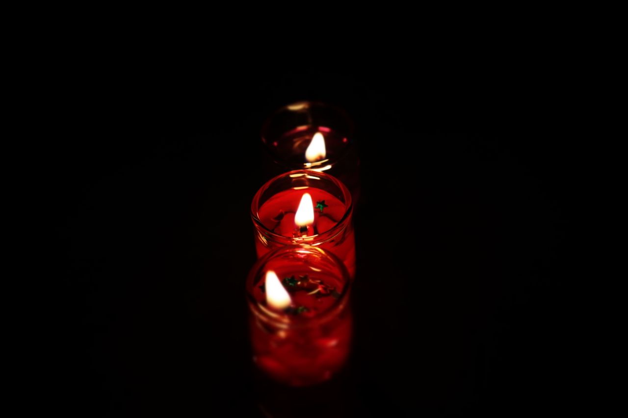 Three glowing red tealight candles in dark setting, creating a warm ambiance.