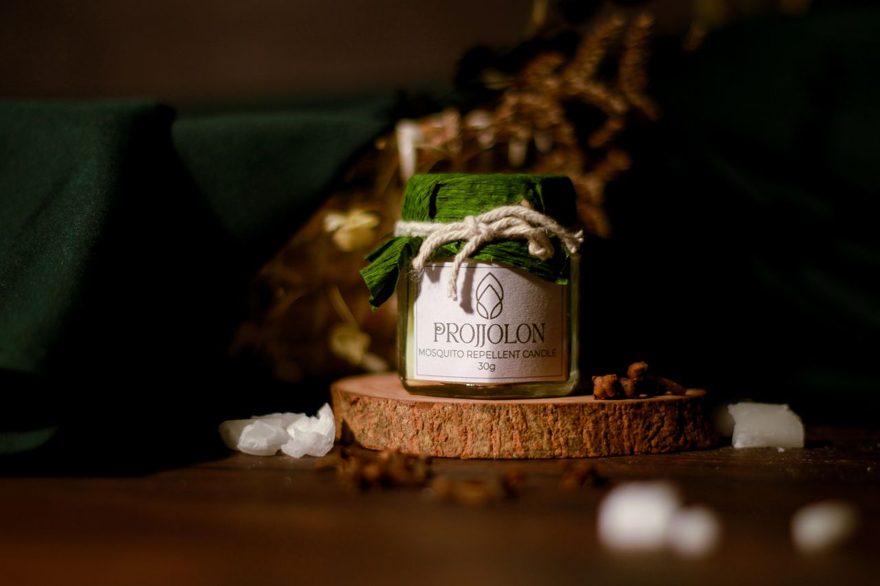 A Projjolon mosquito repellent candle displayed on a wooden base, emphasizing eco-friendly and organic features.